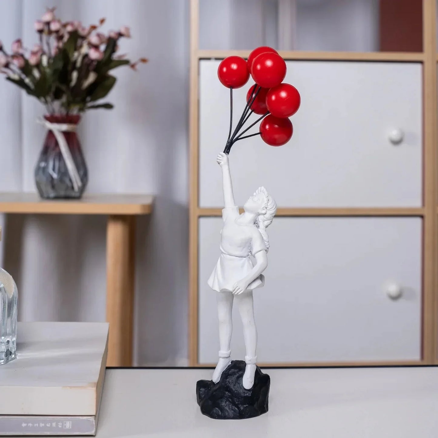 Balloon Girl Resin Statuette sitting on a white shelf with indoor plants and decorative elements in a modern interior setting.