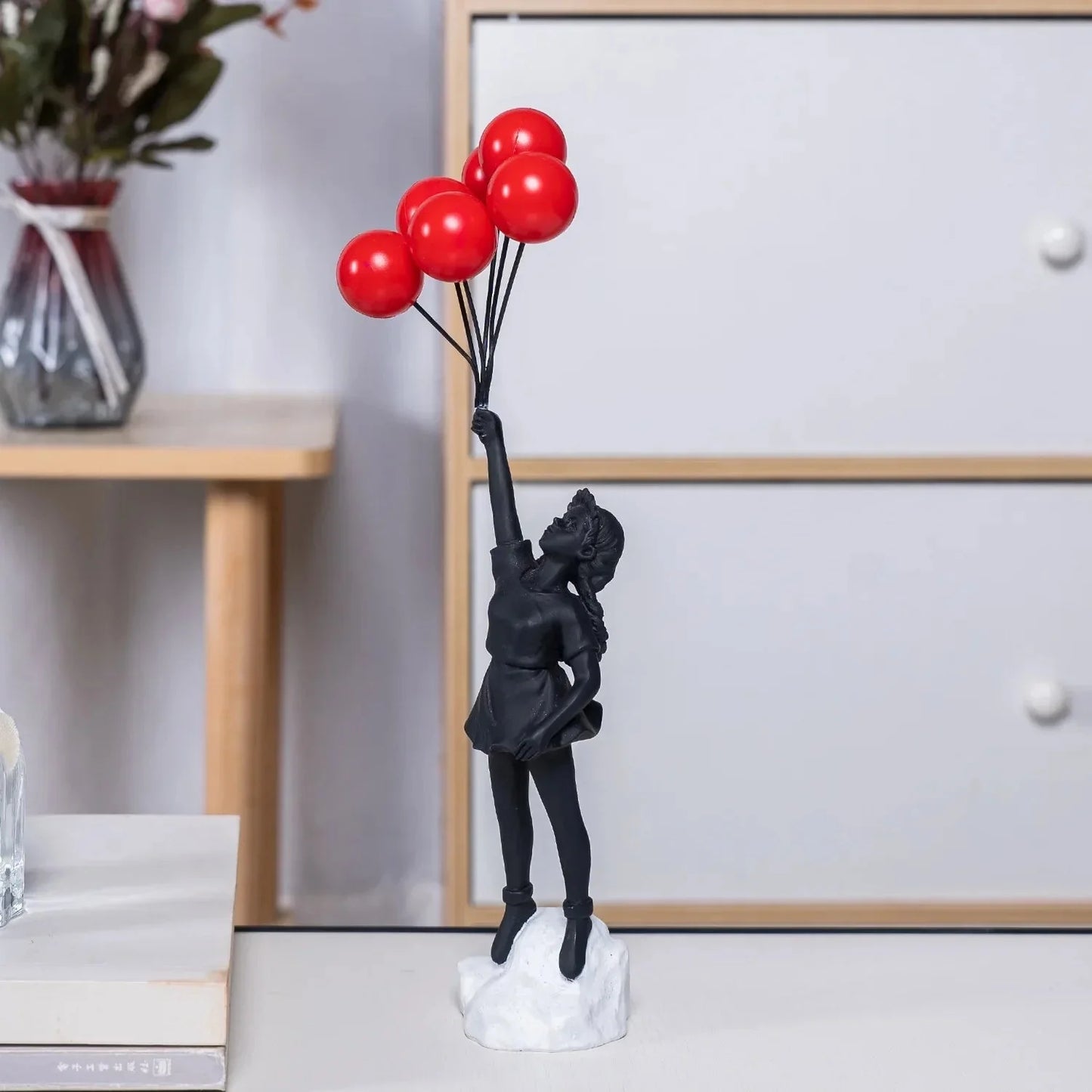 Balloon Girl Resin Statuette depicting a young girl holding a balloon, set against a background with a window and a plant, reflecting an urban art-inspired theme.