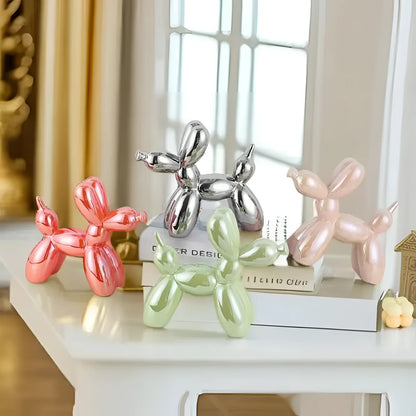 Silver metallic balloon dog sculpture displayed on a wooden surface near a window, with a hint of pink reflection in the background.